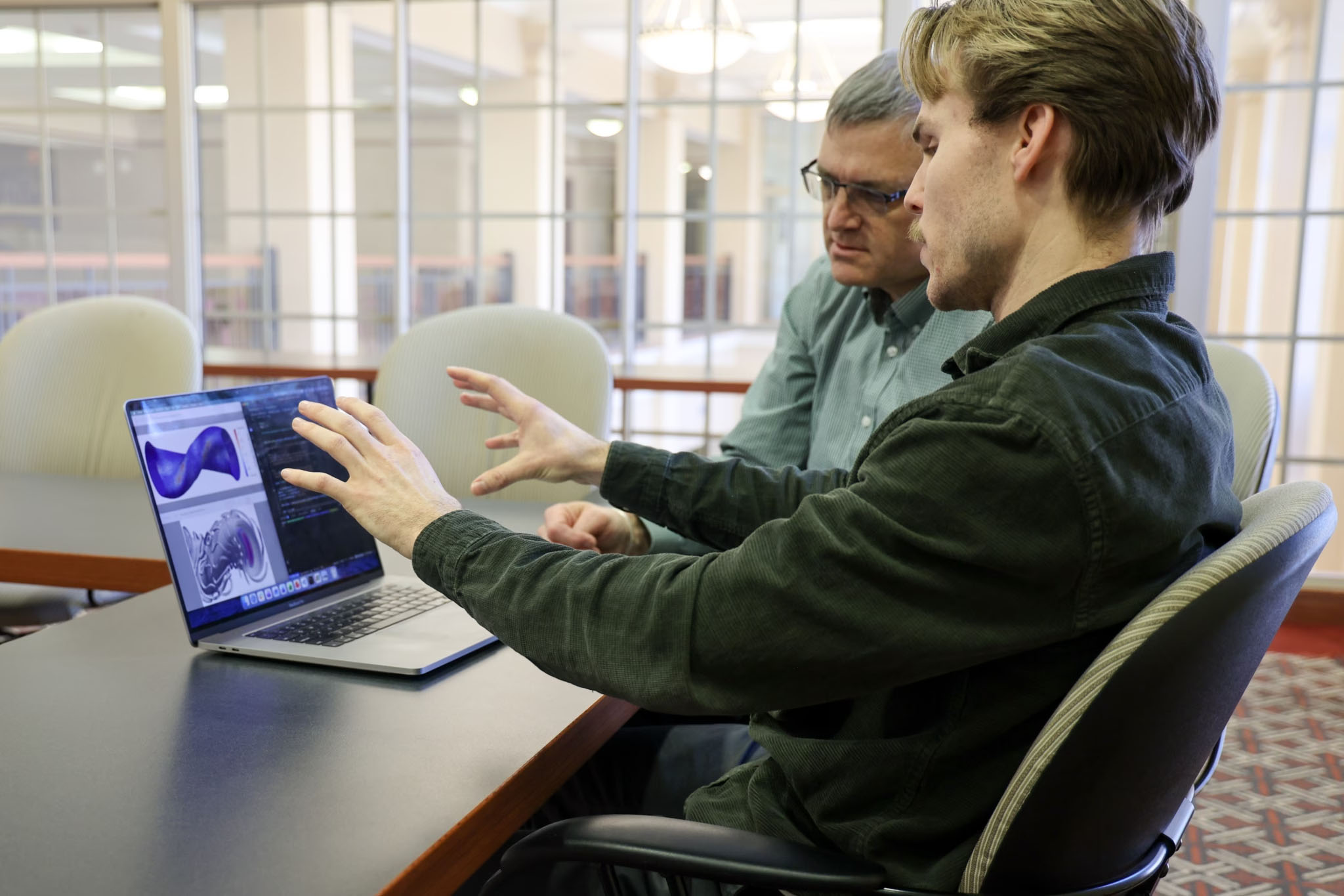 Connor Moreno is a white man with brown hair who is talking with an older man with gray hair about the software tools he developed to help leading fusion companies design the first commercially viable fusion power plants.