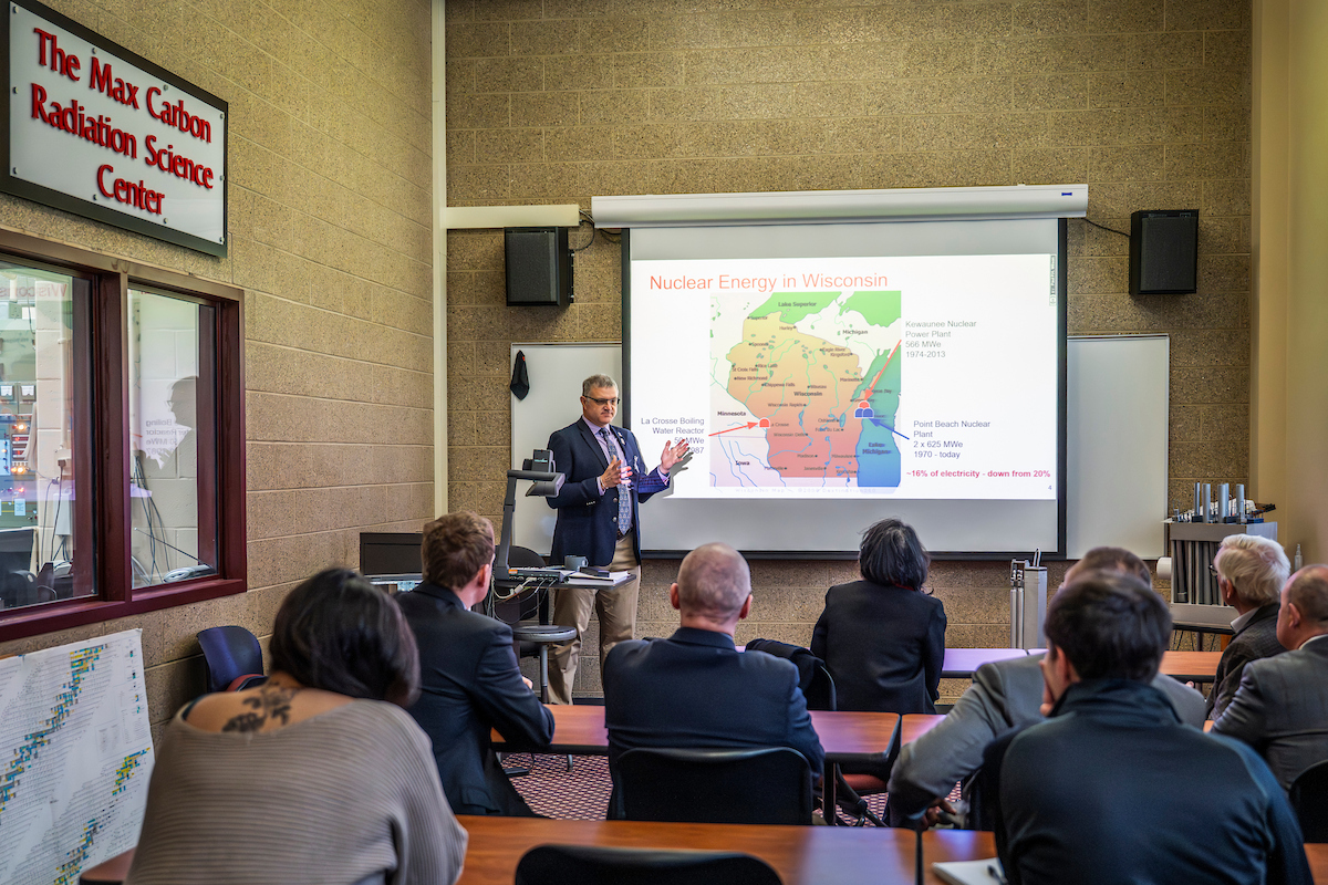 Paul Wilson, a white man with short brown hair, is the Chair of the UW-Madison Department of Nuclear Engineering and Engineering. He is standing in front of a Wisconsin map discussing nuclear energy in Wisconsin to a legislative group